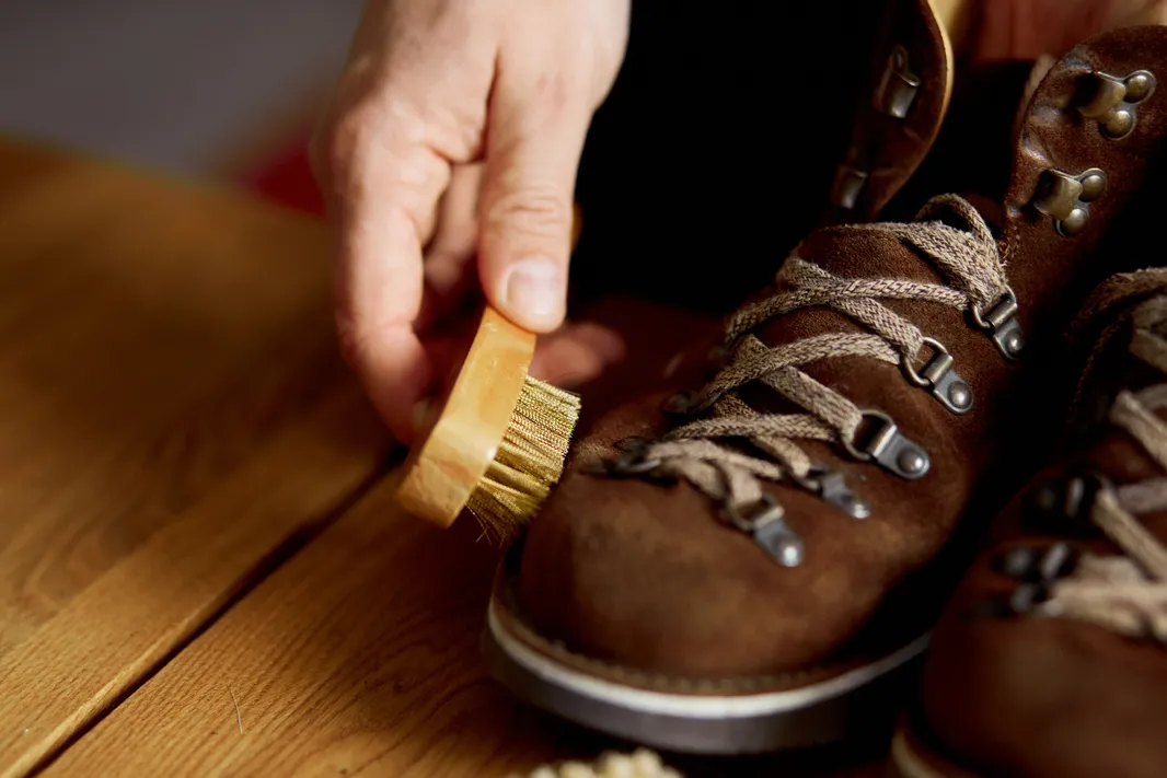 Cómo limpiar botas de piel: Fotografía de una persona cepillando unas botas de piel color café con agujetas beige.
