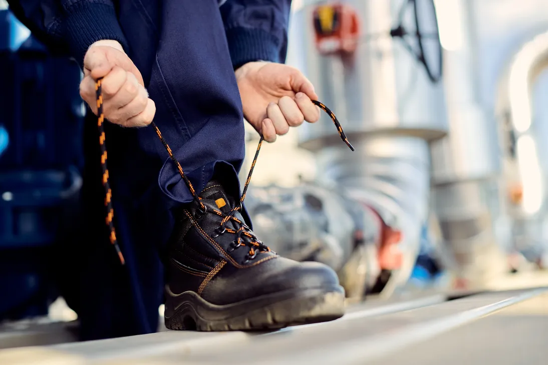 Mejores zapatos de seguridad: Fotografía de un hombre atando los cordones color negro con naranja de sus zapatos.