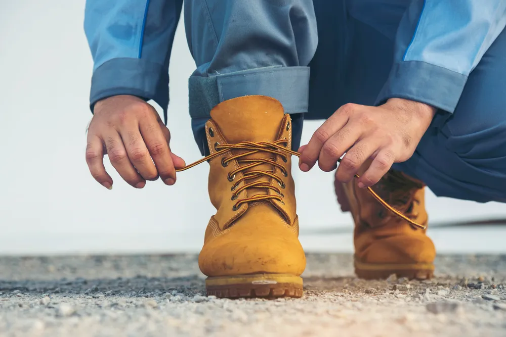Importancia de las botas de seguridad: Fotografía de una persona atando sus botas de seguridad color amarillo.